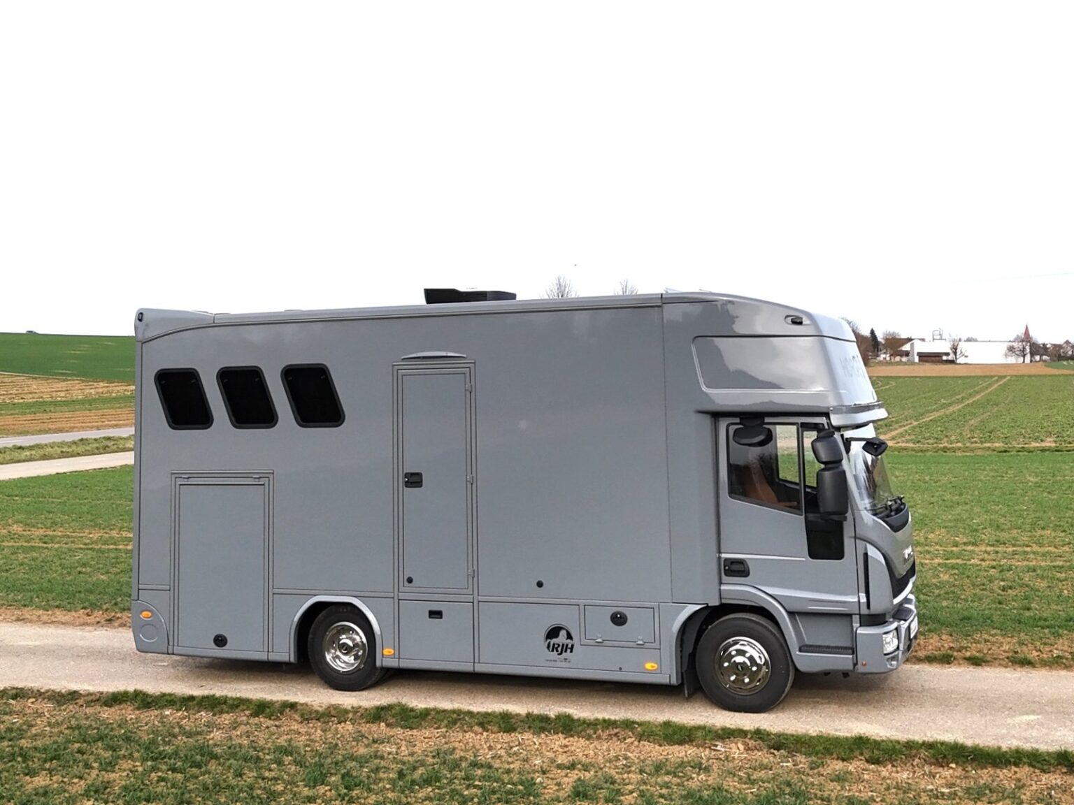 Seitliche Ansicht eines kleinen, grauen Pferdetransporters von RJH auf dem Land