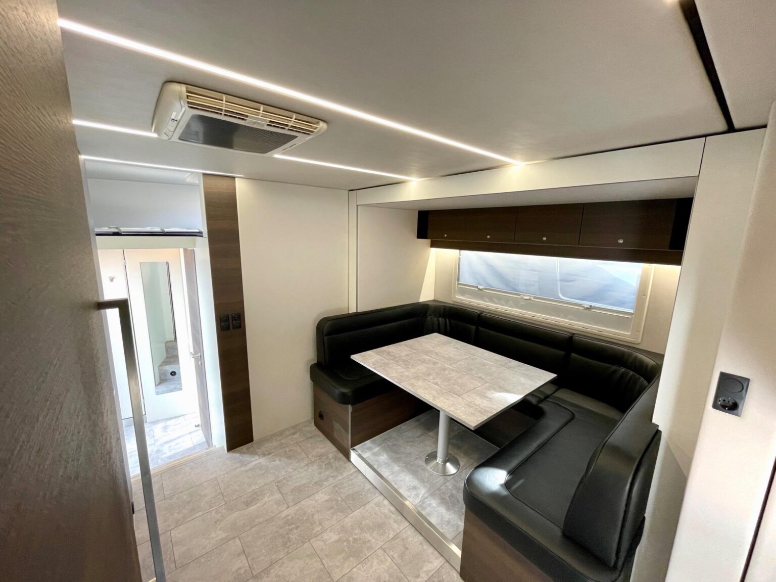 Sitzecke im Wohnabteil des Pferdetransporters mit Tisch in Fliesenoptik, schwarzer Polsterung und Klimaanlage