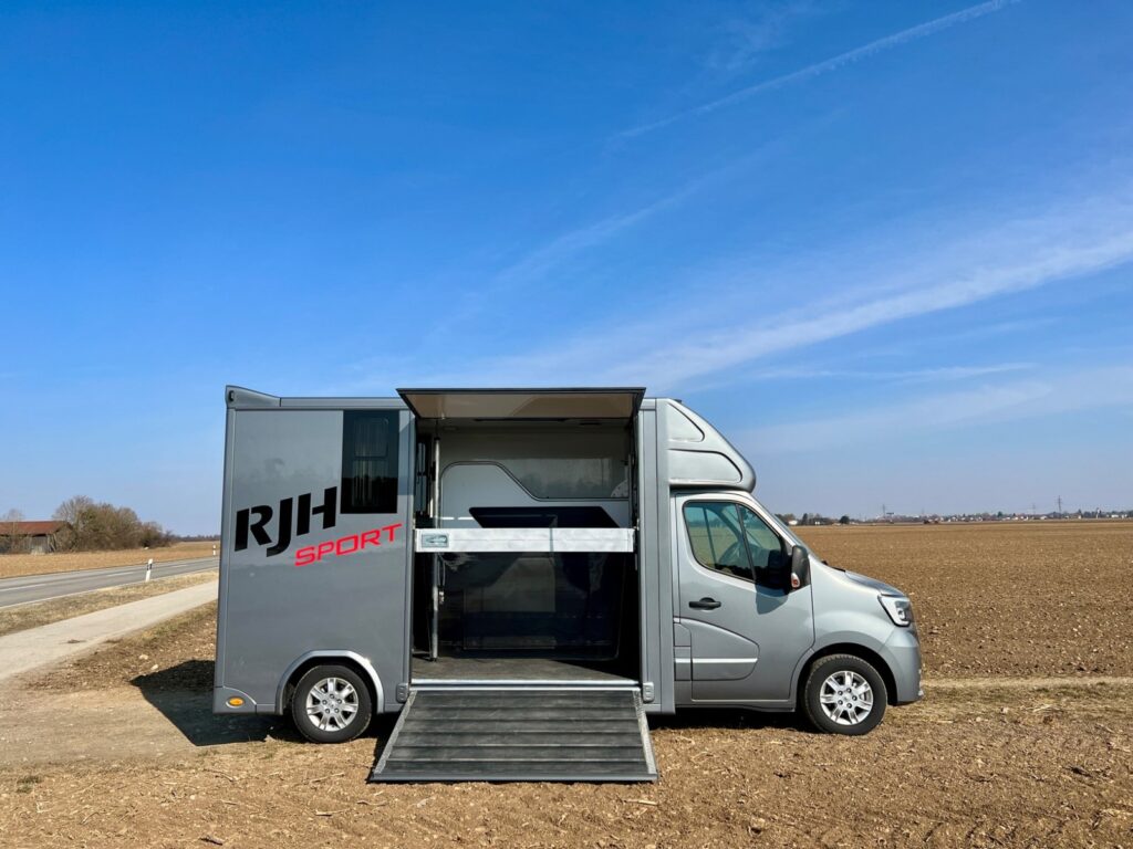 Renault 2-Pferdetransporter steht mit offener Rampe auf einem Feld unter blauem Himmel